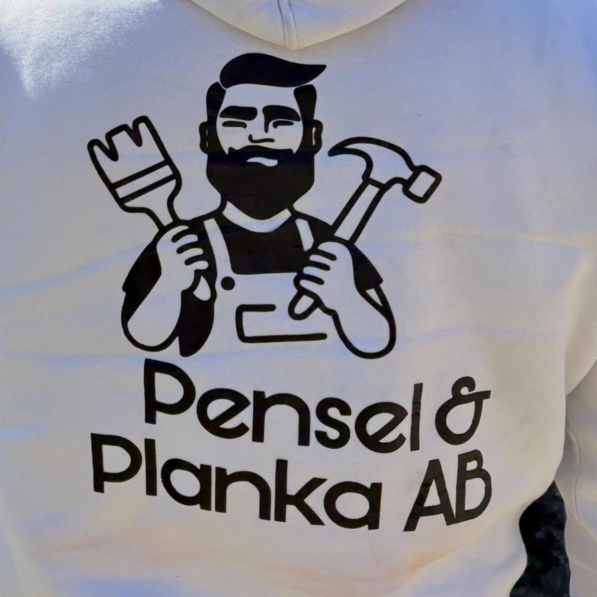 Pensel & Plankas logotyp tryckt på ryggen av en vit hoodie