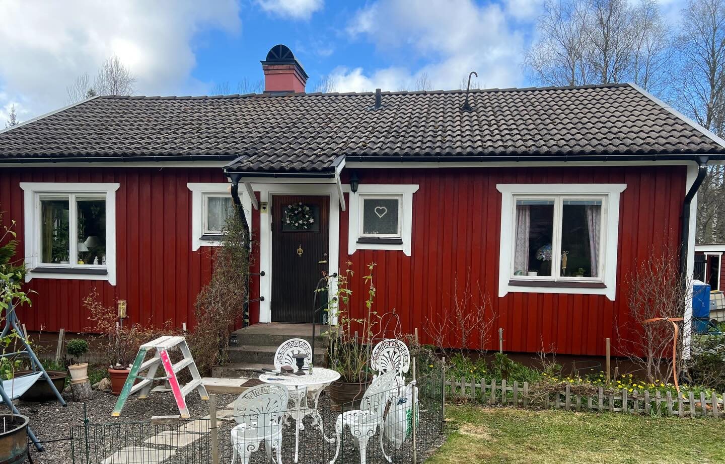 Nymålat rött trähus med vita knutar och fönsterfoder, uteplats framför entrén